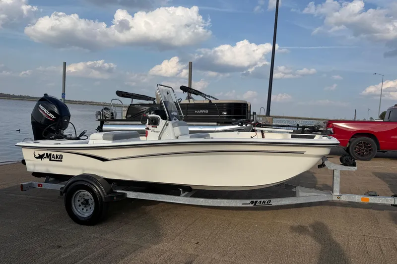 Slide: The Image of 2023 Mako Pro Skiff 15 CC boat on trailer, parked near water under cloudy sky. - 71