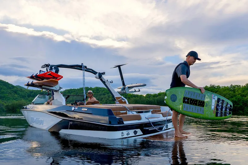 Slide: The Image of Manufacturer Provided Image: 2026 Malibu Wakesetter 21 LX on lake, man holding wakeboard, scenic background. - 2
