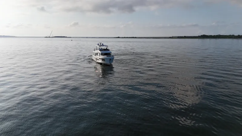 Slide: The Image of 2024 Beneteau Grand Trawler 62 cruising on calm waters under a cloudy sky. - 2