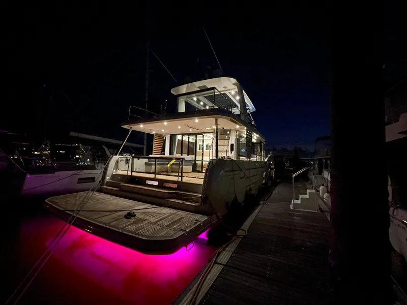 Slide: The Image of 2024 Beneteau Grand Trawler 62 docked at night with vibrant underwater lights. - 20