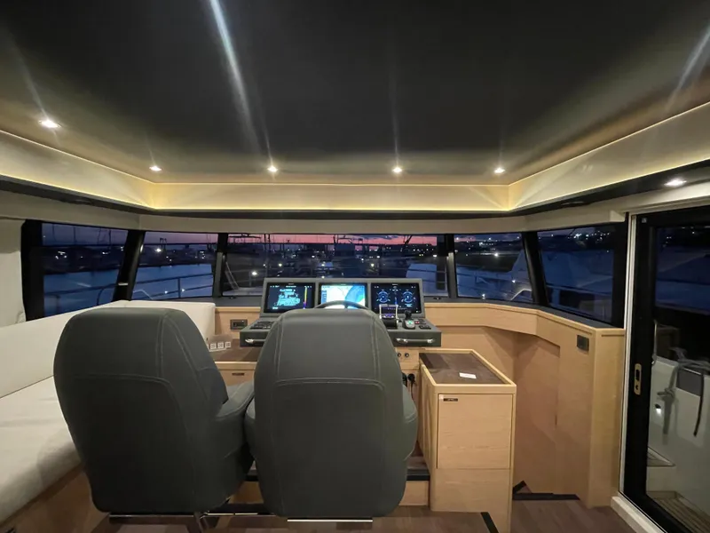 Slide: The Image of 2024 Beneteau Grand Trawler 62 helm with modern controls and panoramic windows at sunset. - 25