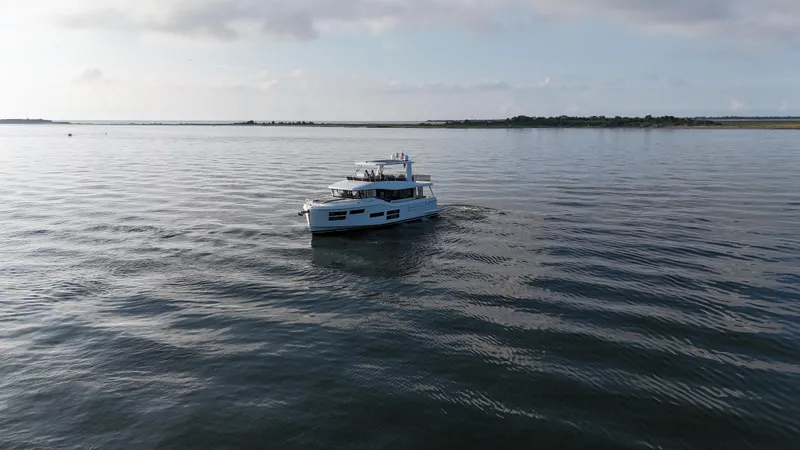 Slide: The Image of 2024 Beneteau Grand Trawler 62 cruising on calm waters under a cloudy sky. - 3