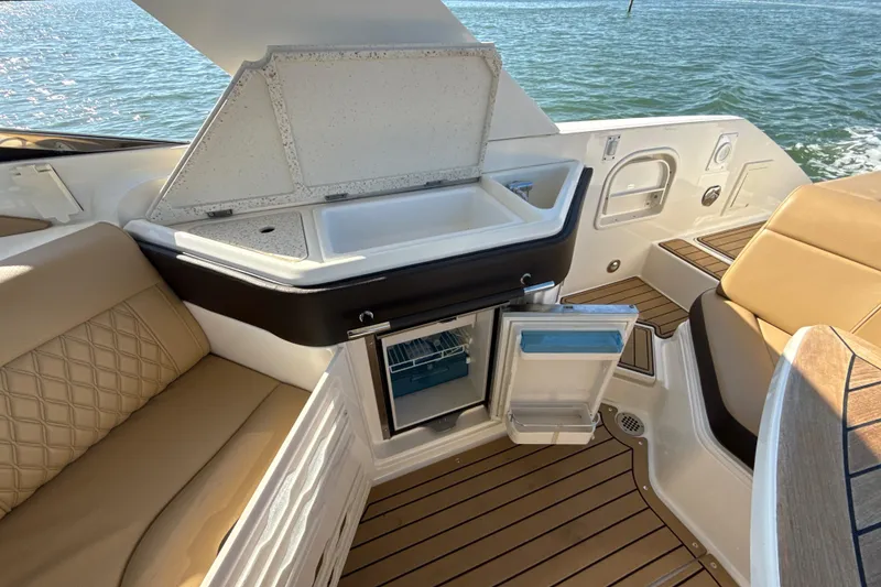 Slide: The Image of 2021 Sea Ray SLX 310 Outboard interior with open fridge and sink, on water. - 19