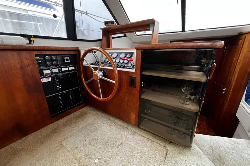 Slide: The Image of 1991 Carver 33 Aft Cabin Motor Yacht helm with wooden steering wheel and glass cabinet. - 26