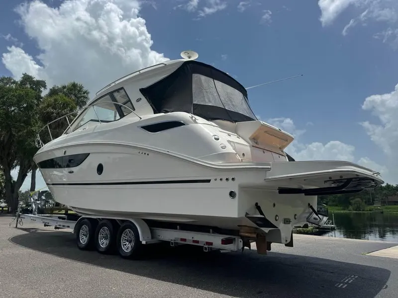Slide: The Image of 2017 Sea Ray Sundancer 350 Coupe on trailer, parked near water under a cloudy sky. - 2