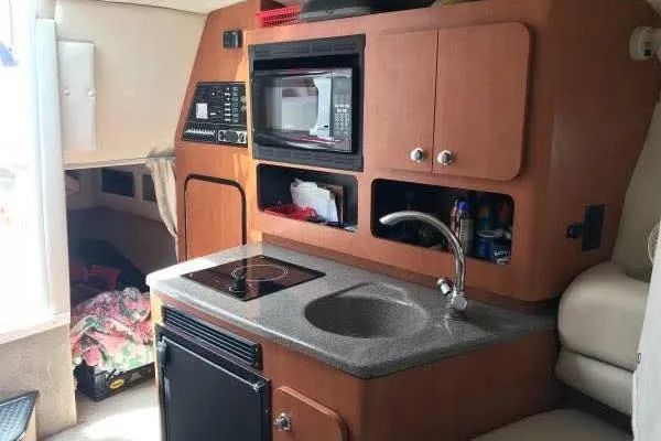 Slide: The Image of 2004 Crownline 270 CR boat interior with kitchenette, featuring sink, stove, microwave, and storage. - 7