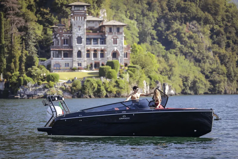 Slide: The Image of 2026 Cranchi E26 Rider boat on scenic lake with historic mansion backdrop. - 15
