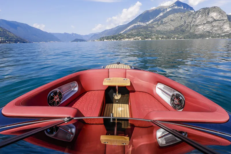 Slide: The Image of 2026 Cranchi E26 Rider boat with red seating, cruising on a scenic lake. - 27