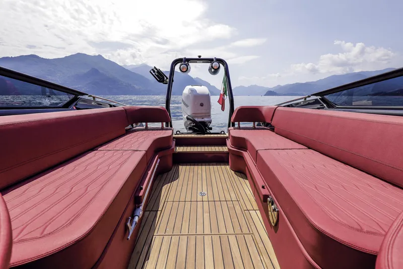 Slide: The Image of 2026 Cranchi E26 Rider boat interior with red seating, wooden deck, and scenic lake view. - 33
