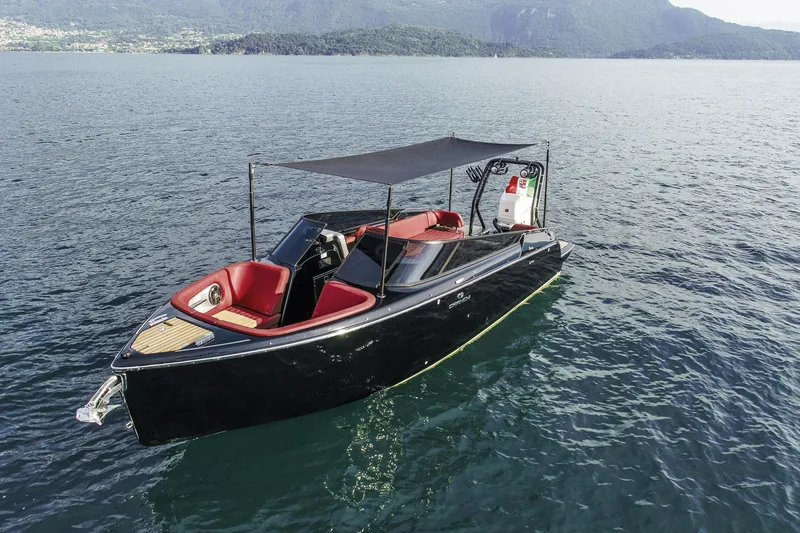Slide: The Image of 2026 Cranchi E26 Rider boat with red seating, black hull, and canopy on a serene lake. - 45