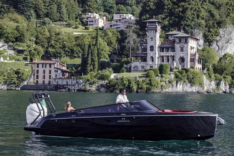 Slide: The Image of 2026 Cranchi E26 Rider boat cruising on a scenic lake with luxurious villas in the background. - 6