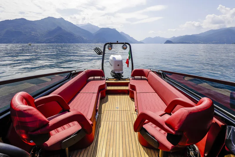 Slide: The Image of 2026 Cranchi E26 Rider boat with red seating, cruising on a serene lake with mountain views. - 9