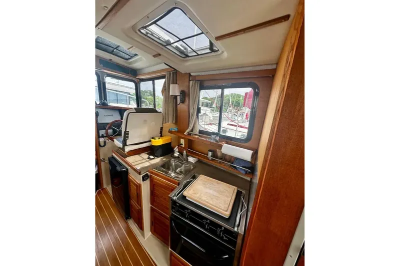 Slide: The Image of 2014 Ranger Tugs R-27 boat interior with kitchenette, featuring wood cabinetry and appliances. - 11