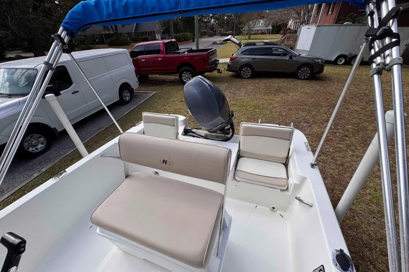 Slide: The Image of 2017 NauticStar 1810 NauticBay boat interior with seating and motor, parked near vehicles. - 10