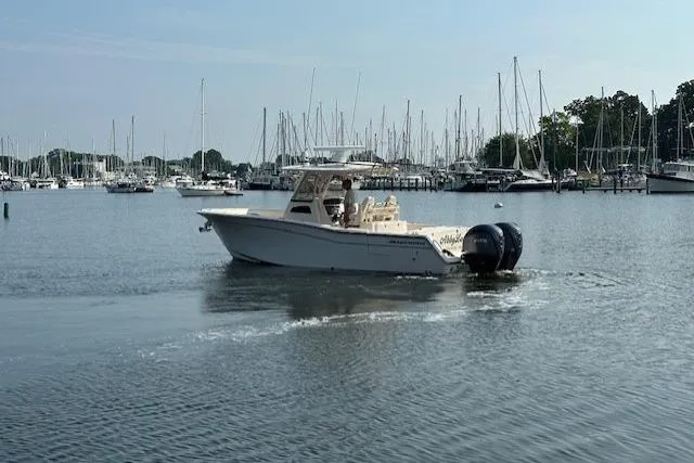 Slide: The Image of 2023 Grady-White Canyon 306 boat cruising in a marina with sailboats in the background. - 2