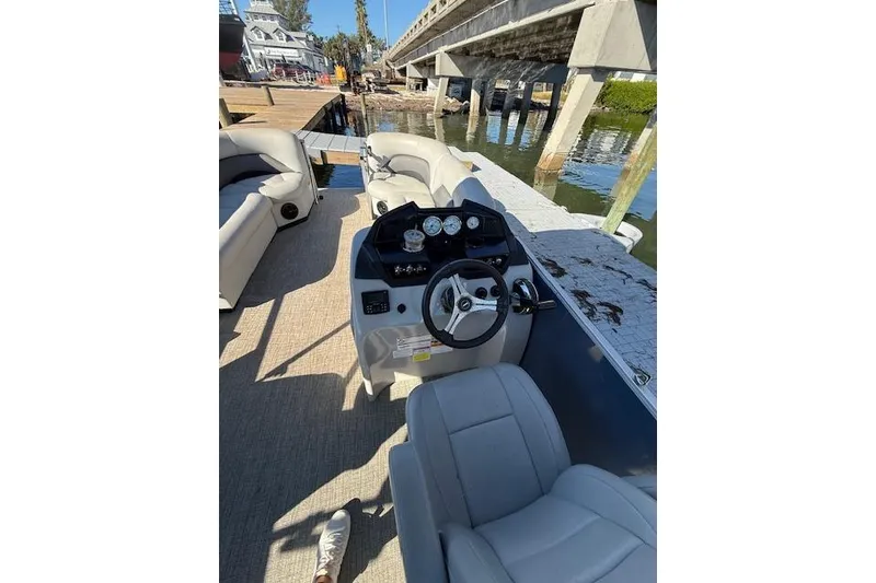 Slide: The Image of 2024 Island Breeze 232 boat interior with steering console and seating, docked near a bridge. - 9