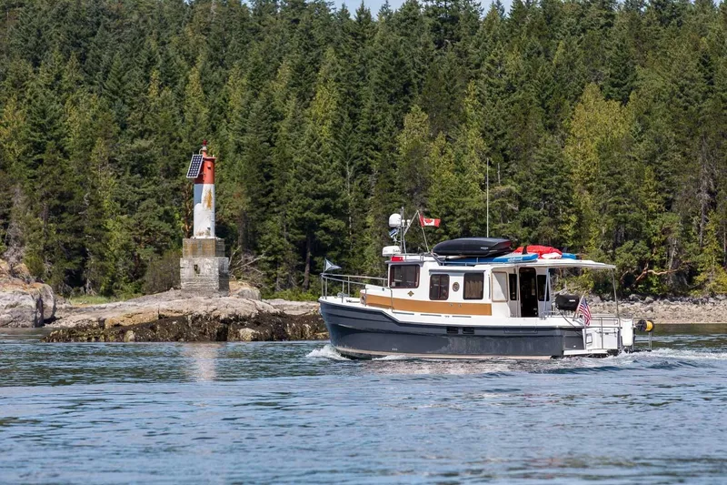 Slide: The Image of 2026 Ranger Tugs R-31S cruising near a small lighthouse, surrounded by lush forest. - 6