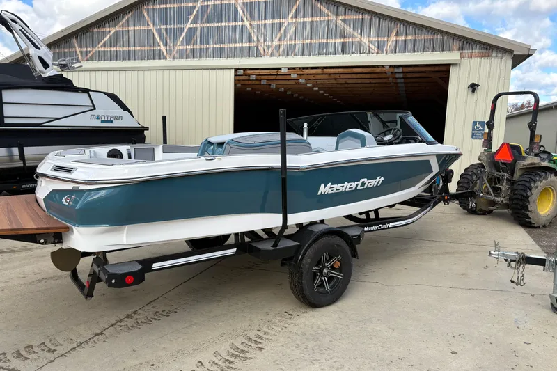 Slide: The Image of 2025 MasterCraft ProStar boat on trailer, parked near a barn and tractor. - 2