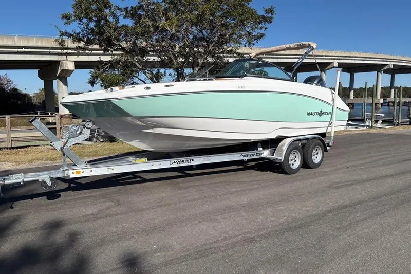 The Image of 2026 NauticStar 223 DC Deck boat on trailer, parked near a bridge. - 1