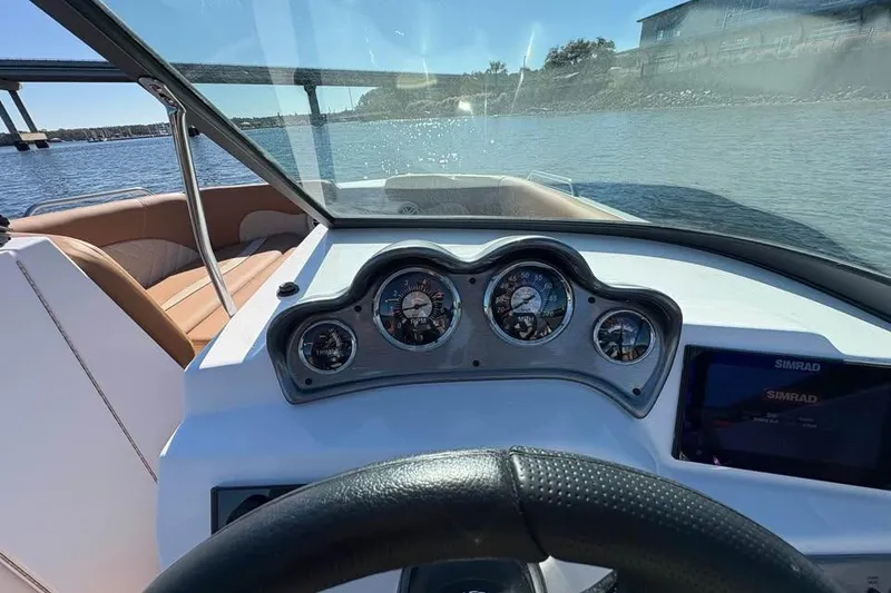 Slide: The Image of 2026 NauticStar 223 DC Deck boat dashboard with gauges and steering wheel on a sunny day. - 12