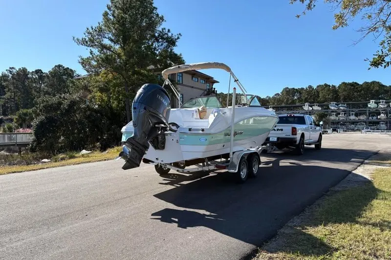 Slide: The Image of 2026 NauticStar 223 DC Deck boat on trailer, towed by a truck, sunny day. - 4