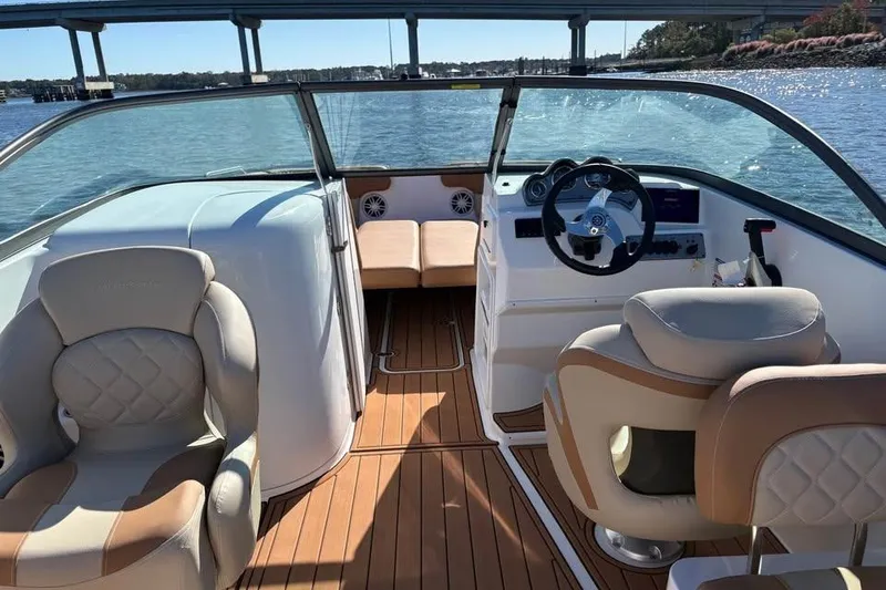 Slide: The Image of 2026 NauticStar 223 DC Deck boat interior with luxurious seating and steering, under a bridge. - 8