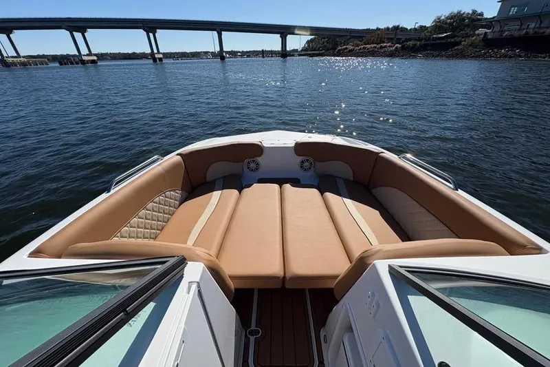 Slide: The Image of 2026 NauticStar 223 DC Deck boat with tan seating, on a sunny day by a bridge. - 9