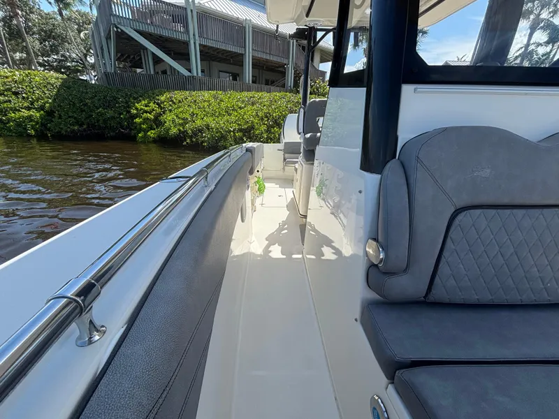 Slide: The Image of 2023 Stingray 273 CC boat interior with gray seating, docked near lush greenery. - 12