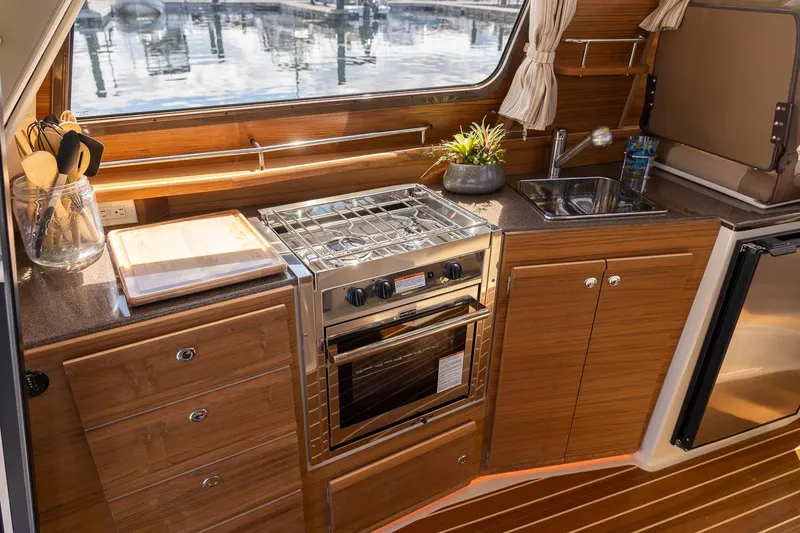 Slide: The Image of 2026 Ranger Tugs R-29CB galley with stove, sink, and wooden cabinetry. - 19