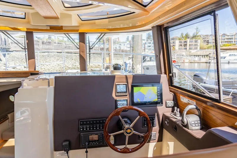 Slide: The Image of 2026 Ranger Tugs R-29CB helm with navigation screens and steering wheel, docked at marina. - 21