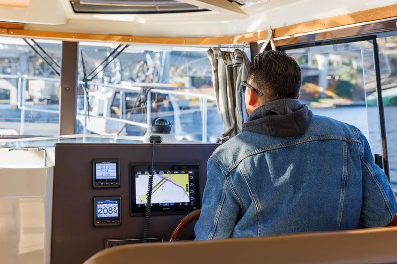 Slide: The Image of Man steering 2026 Ranger Tugs R-29CB boat, viewing navigation screens, wearing denim jacket. - 34