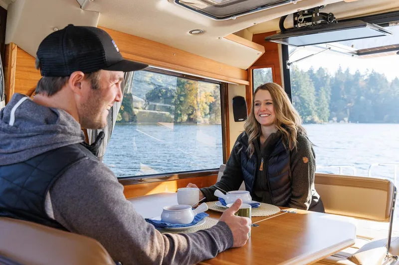 Slide: The Image of Couple enjoying a meal inside a 2026 Ranger Tugs R-29CB boat on a scenic lake. - 36