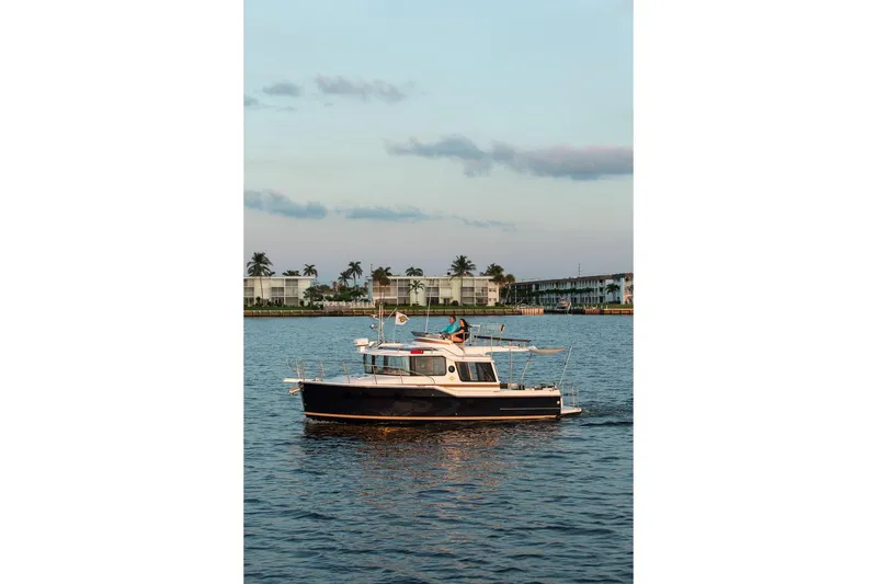Slide: The Image of 2026 Ranger Tugs R-29CB cruising on calm waters near a coastal building. - 39