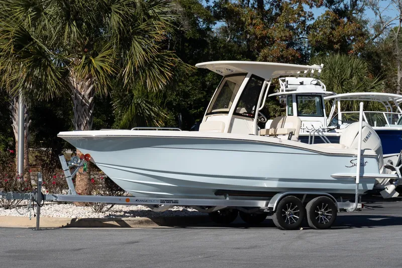 Slide: The Image of 2026 Scout 220 XSF boat on trailer, parked near palm trees. - 2