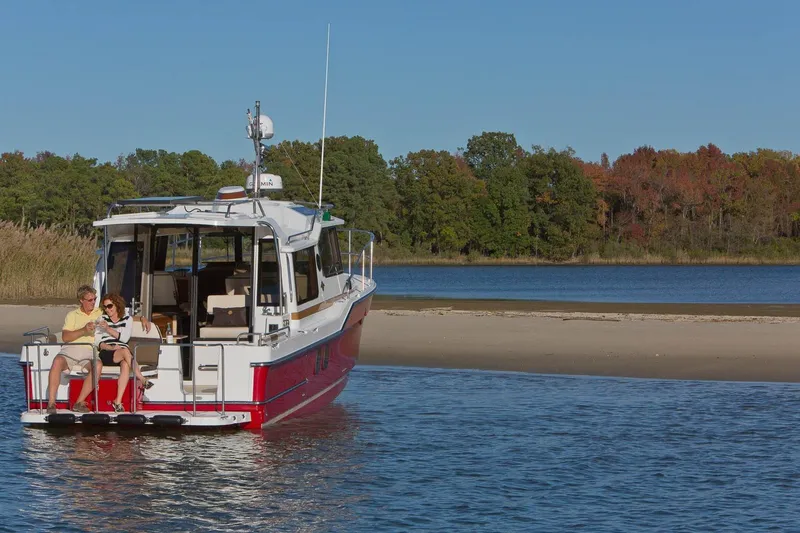 Slide: The Image of 2026 Ranger Tugs R-29S boat anchored near a scenic shoreline with two people relaxing. - 5