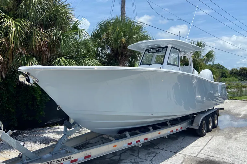 The Image of 2026 Sportsman Open 322 Center Console boat on trailer, surrounded by palm trees. - 0