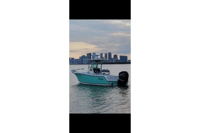 Slide: The Image of 2019 Mako 234 Center Console boat on water with city skyline backdrop. - 6