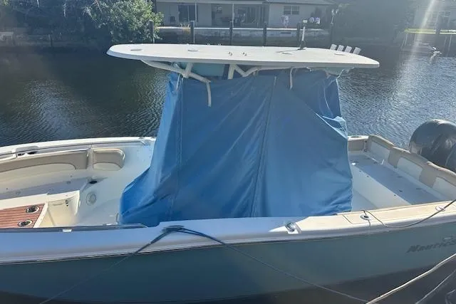 Slide: The Image of 2018 NauticStar 2602 Legacy boat with blue cover docked by the water. - 11