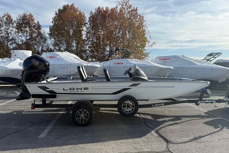 Slide: The Image of 2026 Lowe Outlet 20 boat on trailer, parked outdoors with covered boats in background. - 4