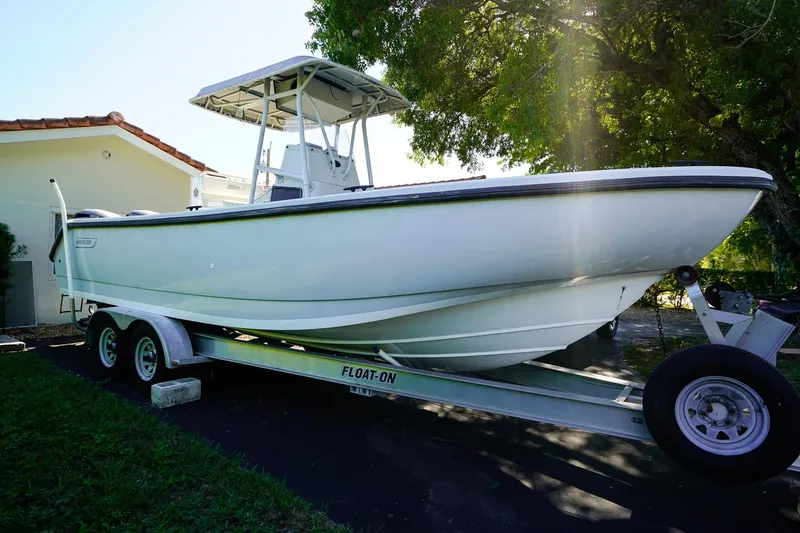 Slide: The Image of 2005 Boston Whaler 260 Justice boat on trailer, parked near house, under sunlight. - 0