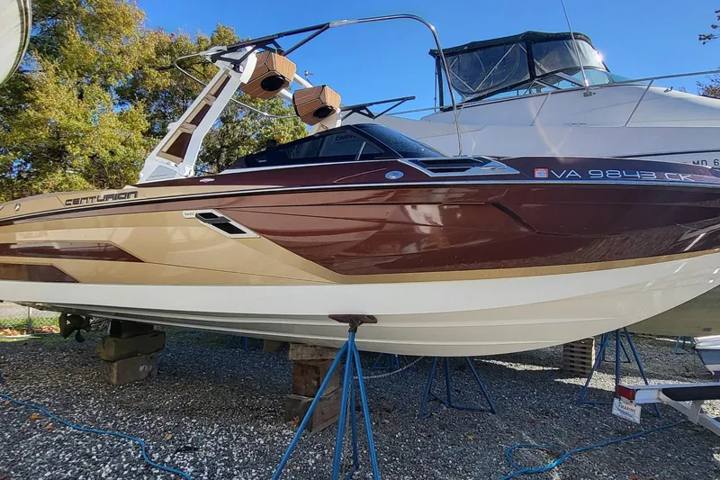 The Image of 2021 Centurion Ri265 boat on stands, brown and white design, outdoor setting. - 1