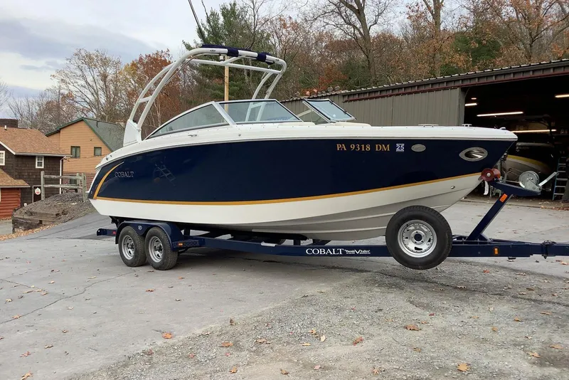 Slide: The Image of 2014 Cobalt R5 boat on trailer, parked outdoors near a garage, surrounded by autumn trees. - 5