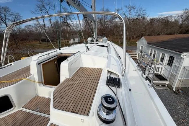 Slide: The Image of 2019 Jeanneau 51 sailboat deck with teak flooring and open hatch, docked near a house. - 48