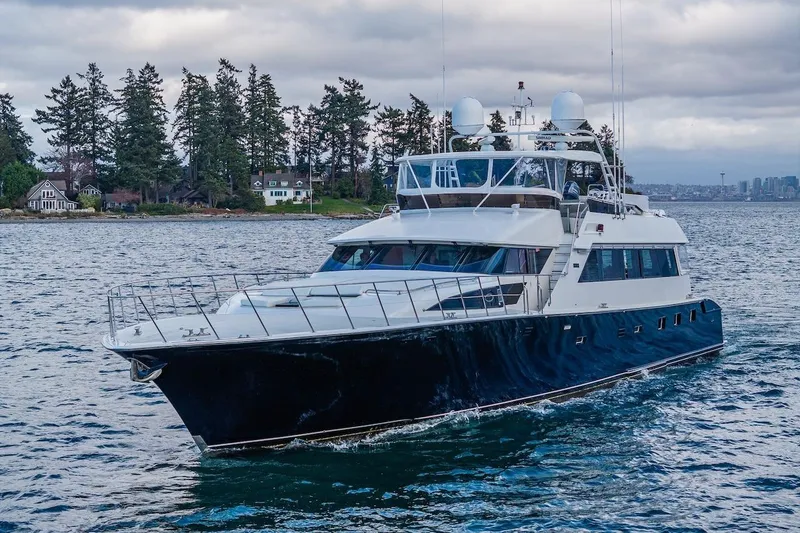 The Image of 1988 Cheoy Lee 92 yacht cruising on a scenic waterway with trees and houses in the background. - 0