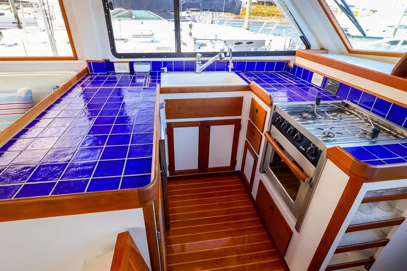 Slide: The Image of 2005 New England Boatworks Downeast Sedan kitchen with blue tiled countertops and wooden cabinetry. - 19