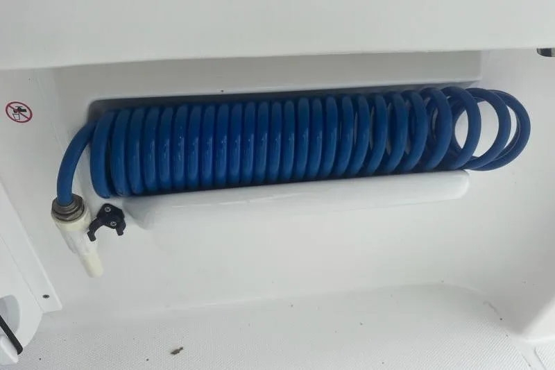 Slide: The Image of Coiled blue hose on 2022 Edgewater 230CC boat, neatly stored in compartment. - 24