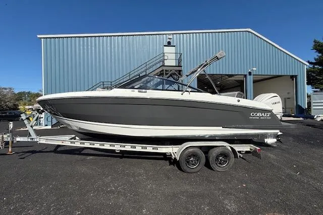 Slide: The Image of 2025 Cobalt R4 Outboard boat on trailer, parked outside a blue warehouse. - 2