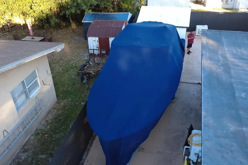 Slide: The Image of Covered 2007 Grady-White Bimini 306 boat in driveway, surrounded by buildings and trees. - 10