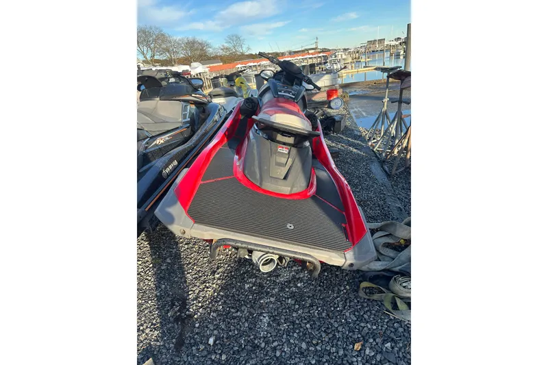 Slide: The Image of 2023 Yamaha WaveRunner VX Deluxe, red and black, parked on gravel near a marina. - 5