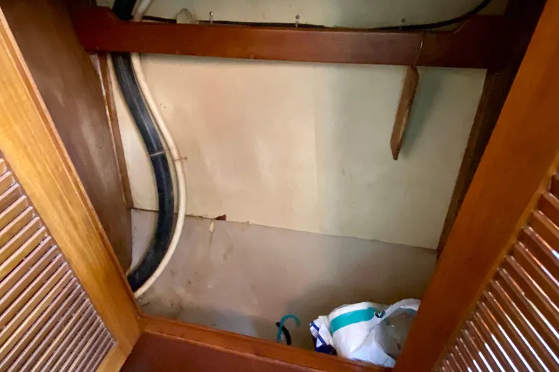 Slide: The Image of Interior storage space on a 1994 Island Packet 44 sailboat, featuring wooden paneling and utility pipes. - 108